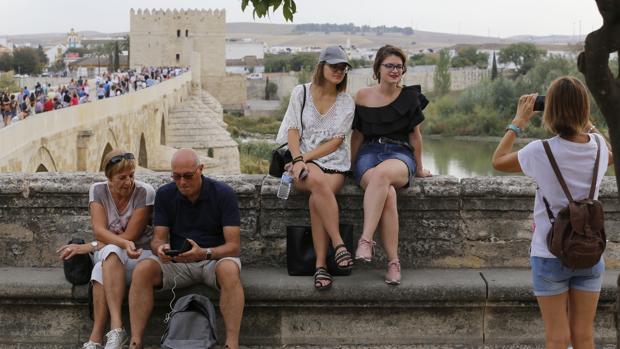 Dos turistas se fotografían con el Puente Romano y la Torre de la Calahorra, al fondo