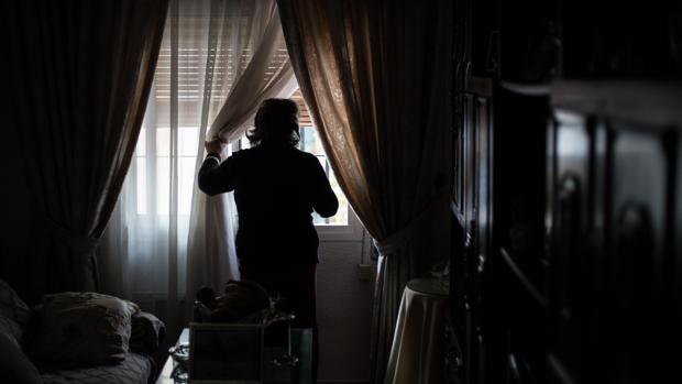 Una mujer de avanzada edad mira a través de la ventana de su vivienda