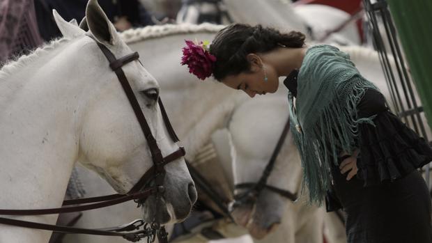 Una joven vestida de flamenca, junto al paseo de caballos