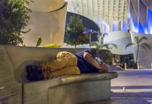 Una persona duerme en un banco en la Plaza de la Encarnación